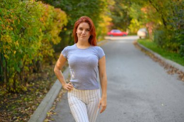 Güzel kızıl saçlı kadın sonbaharda dışarıda poz veriyor..