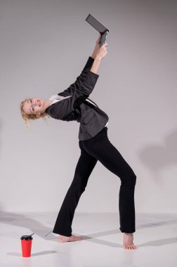 İş elbisesi giymiş çıplak ayaklı balerin dizüstü bilgisayara poz veriyor ve kahve içiyor. Bilgisayar başında esnek bir kadın çalışıyor.