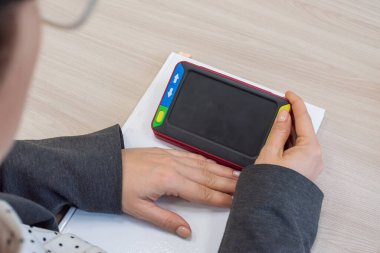 Kadın, görme engelliler için bir okuma cihazı tutuyor. Miyoplar için elektronik büyüteç