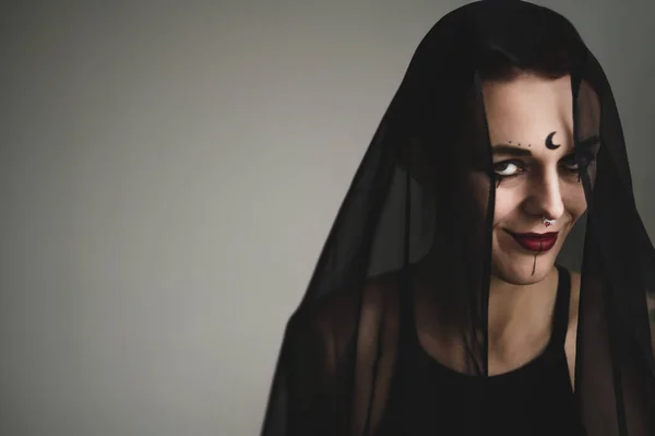 Redhead woman with a black veil on her head in a dark studio. A girl with an earring in her nose smiles slyly. Witch Makeup. Halloween costume. — Stock Photo, Image