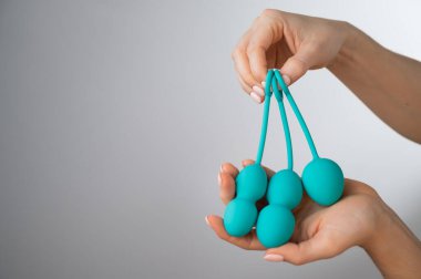 Yüzü olmayan bir kadın bir dizi nane renginde vajinal taşak gösteriyor. Beyaz arka planda pelvik zemin kaslarını çalıştırmak için kegel antrenörü tutan bir kız..