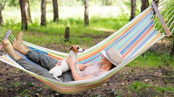 Caucasian woman lies in a hammock with Jack Russell Terrier dog in a pine forest — Stock Photo, Image
