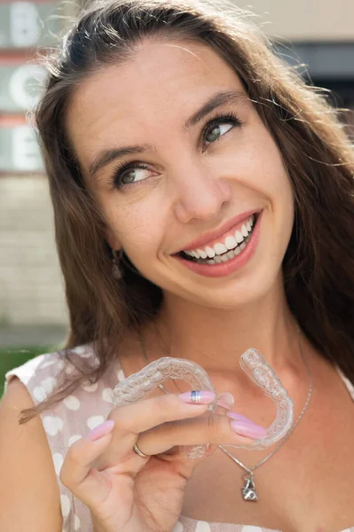 Beautiful caucasian woman holding transparent mouth guards for bite correction. Girl with silicone braces outdoors. — Stock Photo, Image