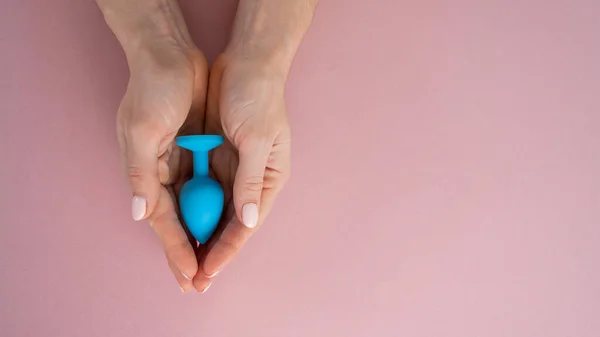 A woman is holding a blue butt plug on a pink background. Adult toy for alternative sex — Foto de Stock