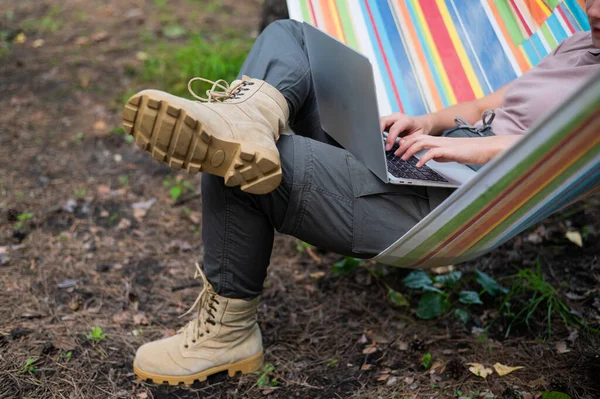 Mulher caucasiana trabalhando em laptop enquanto sentada em uma rede na floresta. Menina usa um computador sem fio em uma caminhada. — Fotografia de Stock