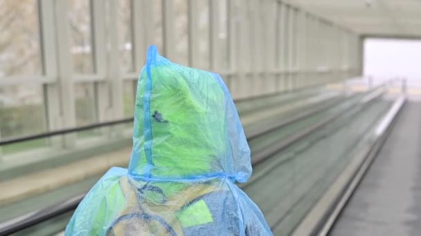 Een vrouw in een regenjas stijgt op op een roltrap. Meisje in beschermende kleding tegen de regen. Achteraanzicht. — Stockvideo