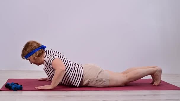 Vieja haciendo flexiones en alfombra deportiva sobre fondo blanco. — Vídeos de Stock