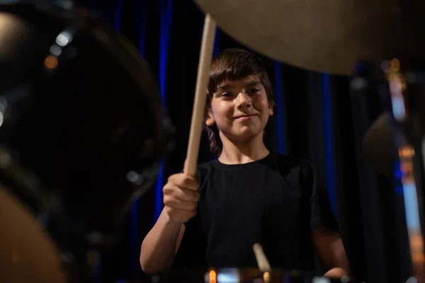 The boy learns to play the drums in the studio on a black background. Music school student