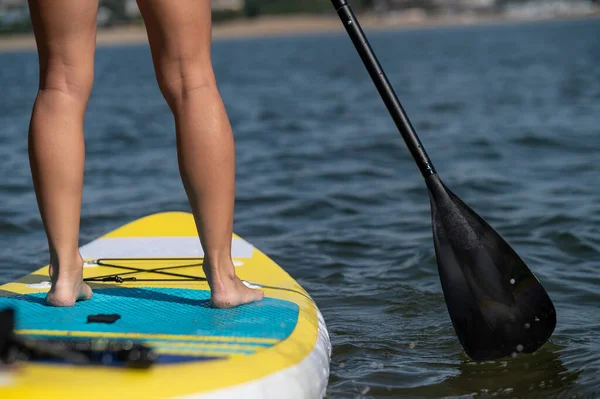 Beyaz bir kadın SUP tahtasının üzerinde yüzüyor. Sörf yaparken kadın bacaklarına yakın çekim. — Stok fotoğraf