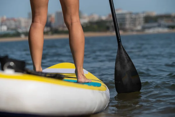 Kaukasierin schwimmt auf einem SUP-Board. Nahaufnahme weiblicher Beine auf der Brandung. — Stockfoto