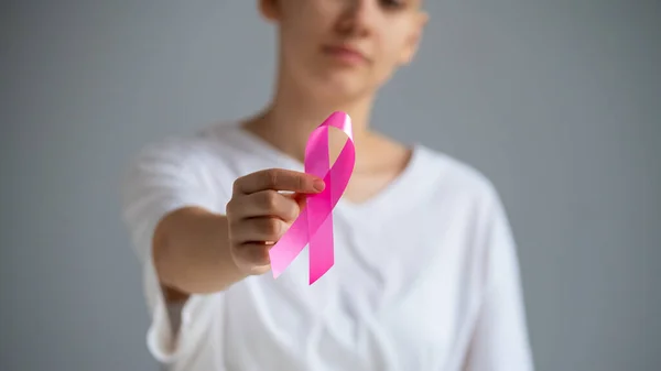 Uma mulher sem rosto usando uma camiseta branca segura uma fita rosa como um símbolo de câncer de mama em um fundo branco. — Fotografia de Stock