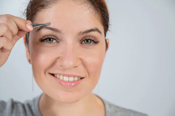 Retrato de close-up de uma mulher caucasiana fazendo correção de sobrancelha com pinças — Fotografia de Stock