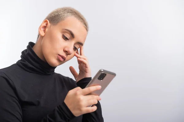 Mujer caucásica joven con el pelo corto utiliza un teléfono inteligente sobre un fondo blanco. — Foto de Stock