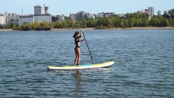 Mulher caucasiana está montando um SUP bordo no rio na cidade. Desporto de verão. — Vídeo de Stock