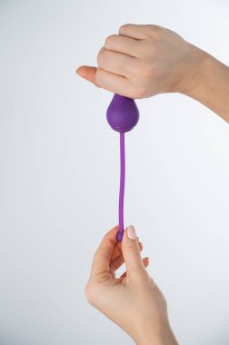 Beyaz arka planda pelvik zemin kaslarını çalıştırmak için elektronik Kegel antrenörü tutan yüzü olmayan bir kadın. Seks oyuncağı akıllı telefonla senkronize edildi