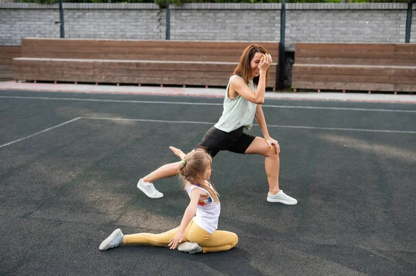 Kaukasiska kvinnor går in för sport med sin dotter utomhus. En skolflicka och hennes mamma springer runt på stadion.. — Stockfoto