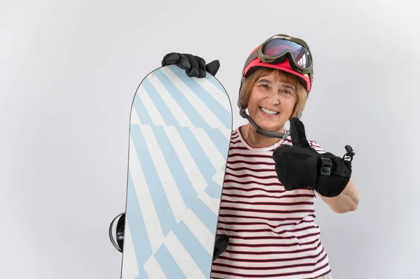 Portrait of smiling elderly woman in ski equipment showing thumb up on white background