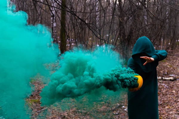 Μια ανατριχιαστική μάγισσα κρατά μια κολοκύθα στον ατμό σε ένα βαθύ δάσος. Jack o φανάρι με πράσινο καπνό για αποκριές — Φωτογραφία Αρχείου