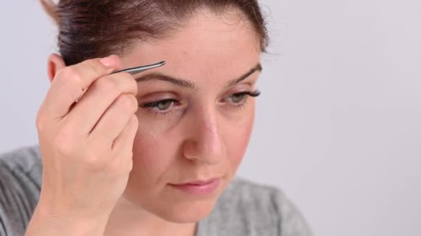 Vit kvinna ser sig själv i spegeln och gör ögonbrynskorrigering med pincett — Stockvideo