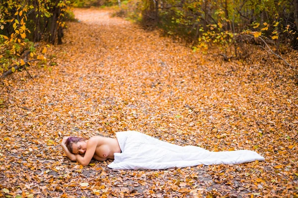 Kaukasische Frau liegt im Herbstwald unter einer Decke. Nacktes Mädchen in einem Blatt fallen — Stockfoto