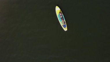 Gölde SUP sörf tahtası süren beyaz bir kadın. Yukarıdan bak. Yaz sporu