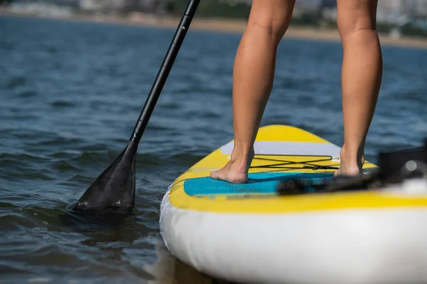 Blanke vrouw zwemt op een SUP bord. Close-up van vrouwelijke benen op de branding. — Stockfoto