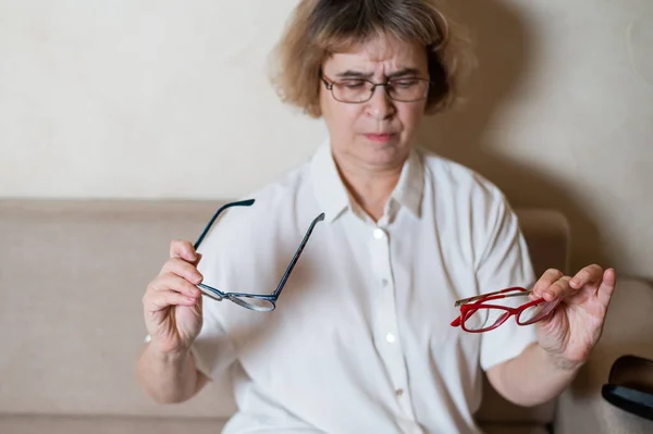 Une femme caucasienne âgée choisit des lunettes de sa collection à la maison — Photo
