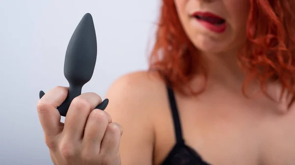 Excited red-haired woman in underwear holds a black butt plug in her hands on a white background — Stock Fotó