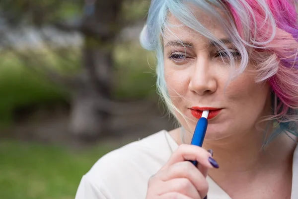 Vit kvinna med färgat hår röker en elektronisk cigarett. — Stockfoto