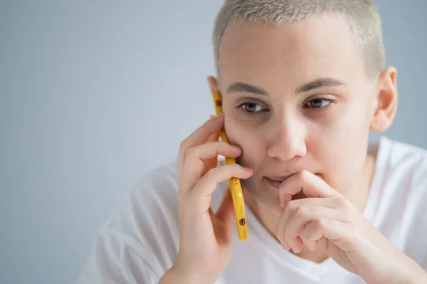 Una joven pensativa con un corte de pelo corto habla pensativamente en un teléfono móvil sobre un fondo blanco — Foto de Stock