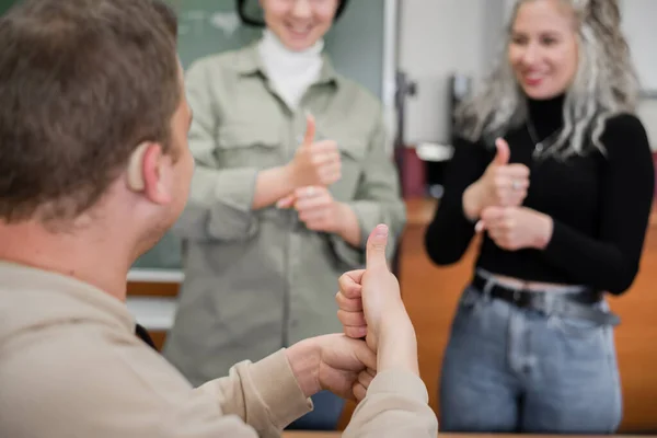 Две девушки и парень разговаривают на языке жестов. Трое глухих студентов общаются в университетском классе. — стоковое фото