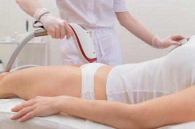 Profesyonel güzellik salonundaki bir kadın, lazer tüyü çıkararak bikini bölgesindeki istenmeyen bitkileri temizliyor.