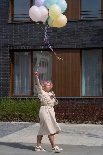 Kvinna i färgat hår promenader med en armfull av ballonger och dricker en uppfriskande dryck — Stockfoto