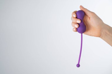 Beyaz arka planda pelvik zemin kaslarını çalıştırmak için elektronik Kegel antrenörü tutan yüzü olmayan bir kadın. Seks oyuncağı akıllı telefonla senkronize edildi