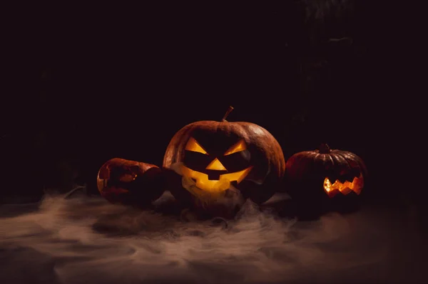 Pumpar med snidade grimaser och ljus inne i mörkret för halloween. Jack o latern i rök. — Stockfoto