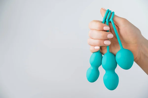 A faceless woman demonstrates a set of mint-colored vaginal balls. Girl holding a kegel trainer for training pelvic floor muscles on a white background. — Stock Photo, Image