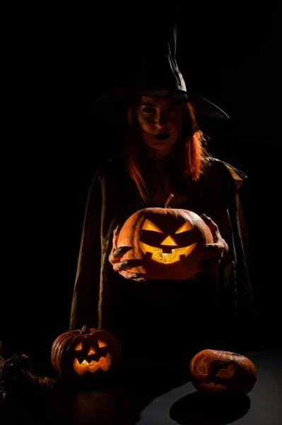 Zła wiedźma rzuciła zaklęcie na dynie. Portret kobiety w karnawałowym kostiumie halloween w ciemności — Zdjęcie stockowe