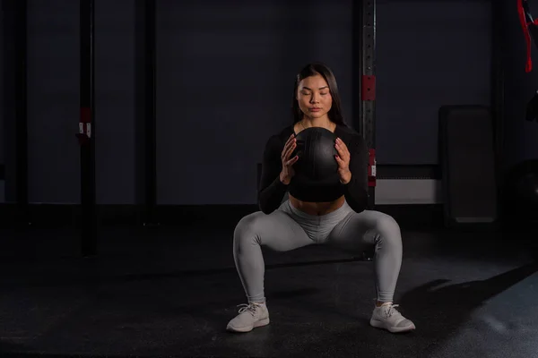 Mujer asiática en cuclillas con una pelota de medicina en el gimnasio. —  Fotos de Stock
