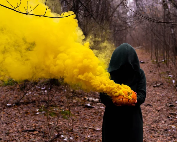 Una strega raccapricciante tiene una zucca fumante in una foresta profonda. Jack o lanterna emette fumo giallo per Halloween — Foto Stock