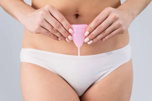 Close-up van een vrouw in wit katoenen slipje met een roze menstruatiecup tegen een witte achtergrond. Alternatief voor tampons en pads — Stockfoto