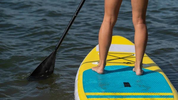 Mujer caucásica nada en una tabla de SUP. Primer plano de las piernas femeninas en el surf. —  Fotos de Stock