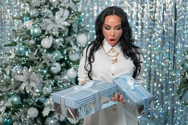 Sexy Brünette im weißen Kleid hält Geschenke am Weihnachtsbaum — Stockfoto