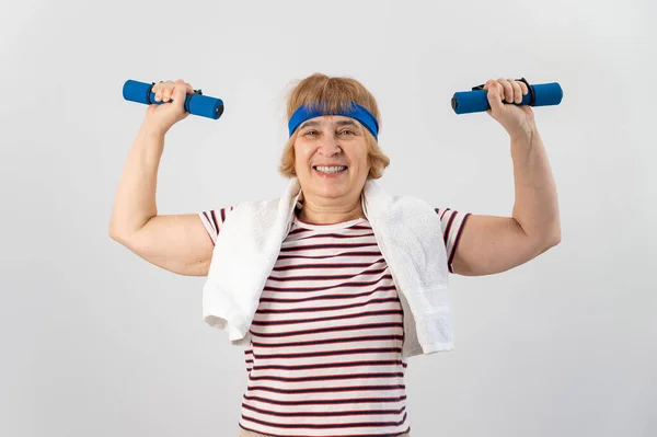 Una anciana con un vendaje azul en la cabeza entrena con pesas sobre un fondo blanco —  Fotos de Stock