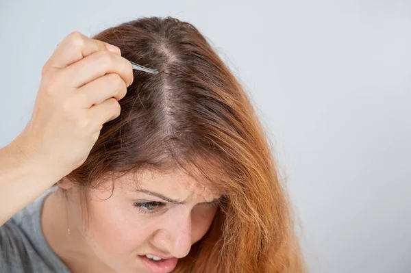 Mujer caucásica encuentra el pelo gris y lo quita con pinzas. Signos de envejecimiento. — Foto de Stock