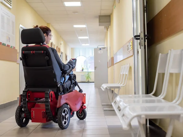 Caucasian woman in electric wheelchair in university corridor.