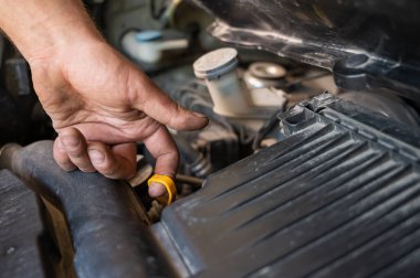 Bir otomobil tamircisi bir araba motorunun yağ seviyesini kontrol etmek için bir çubuk çıkarır..