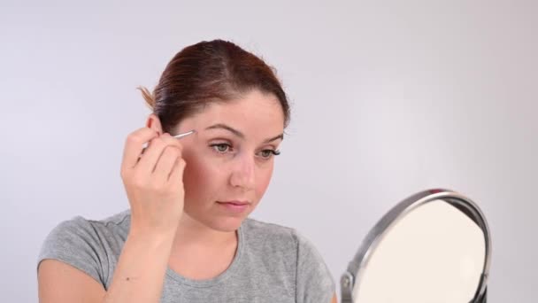 Donna caucasica si guarda allo specchio e fa la correzione del sopracciglio se stessa con pinzette — Video Stock
