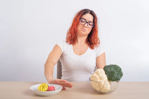 Femme caucasienne préfère la nourriture saine et refuse la restauration rapide. rousse fille choisit entre brocoli et beignets sur fond blanc — Photo