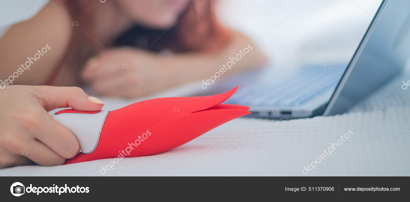 A woman lies in bed holding a clitoral vibrator and watching porn on a laptop photo pic