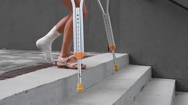 Ayağı kırık bir kadın koltuk değnekleriyle merdivenlerden iniyor.. — Stok video